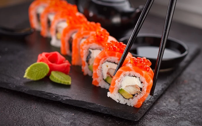 lots of sushi rolls with salmon arranged on black cutting board how to make sushi picked up with black chopsticks