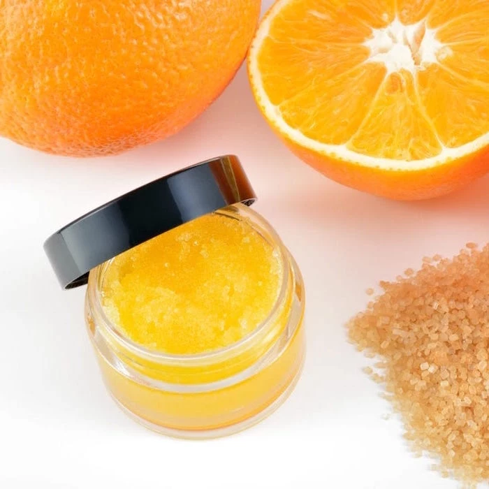 natural orange homemade lip scrub put inside small plastic container with black lid brown sugar and oranges around it