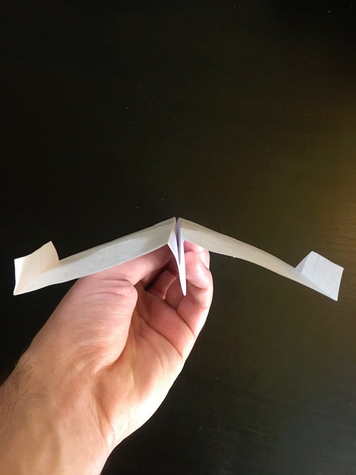 paper airplane folding hand holding a white piece of paper folded into plane photographed from above
