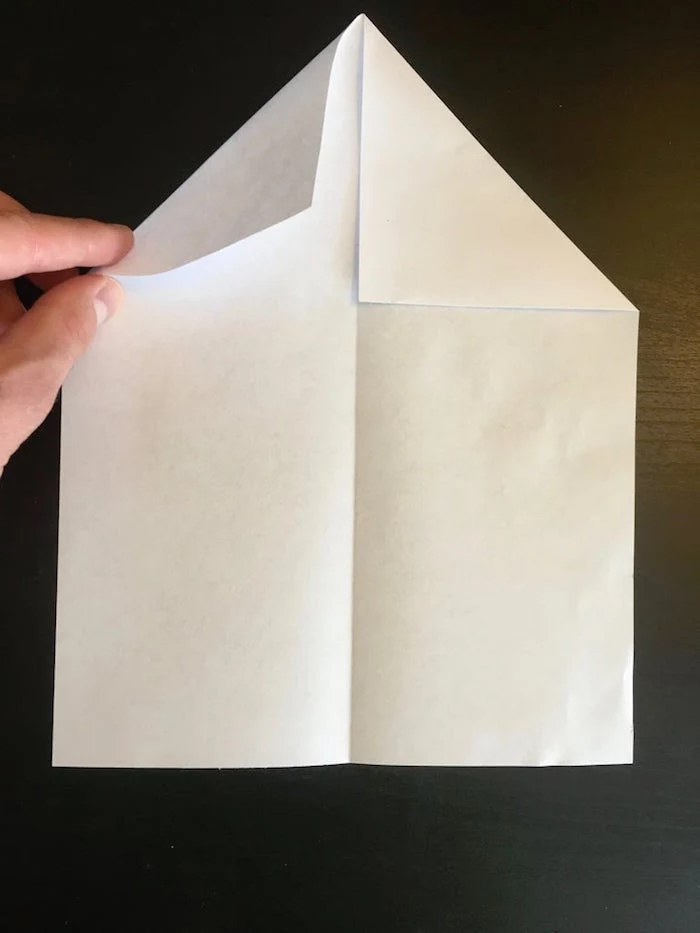 piece of paper with corners folded in placed on black surface paper airplane folding step by step diy tutorial