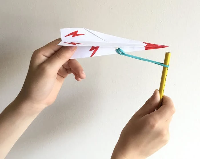 plane tied to pencil with rubber band simple paper airplane white paper folded into plane red flashes drawn on it red tip