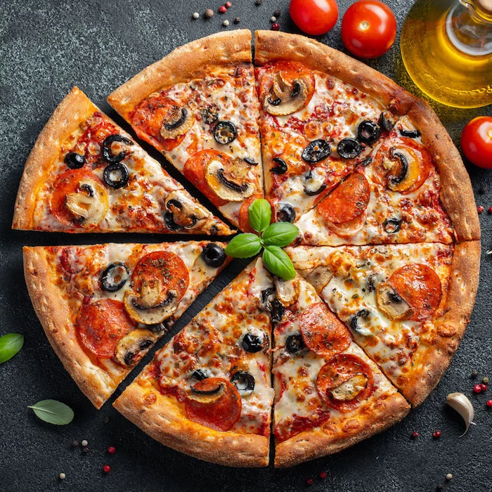 round pizza cut into slices best pizza dough recipe with pepperoni olives mushrooms garnished with fresh basil leaves