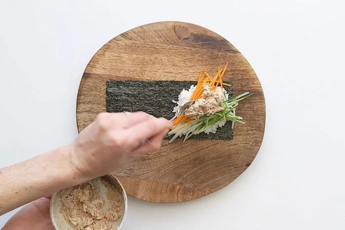 round wooden cutting board how to cook sushi rice nori spread out on it with white rice cucumbers avocado carrots