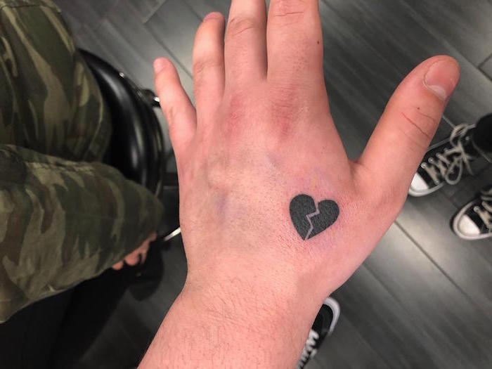 small black heart broken in the middle filled with black ink heart tattoo on chest hand tattoo below the thumb