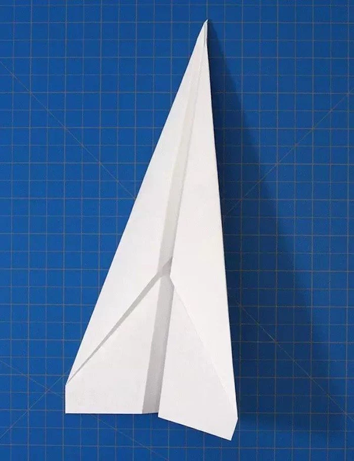 step by step paper airplane diy tutorial of white piece of paper on blue background being folded into a plane