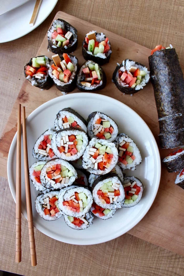 sushi rolls arranged on white plate wooden chopsticks on the side how to make sushi rice placed on wooden cutting board