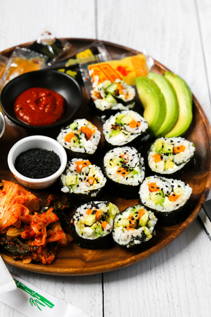 sushi rolls arranged on wooden tray california roll recipe with avocado black sesame seeds different types of sauce