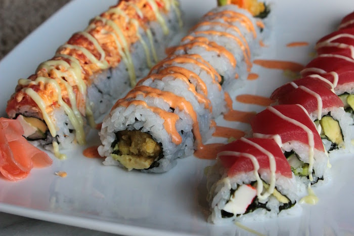 three different types of sushi arranged on white tray shrimp tempura roll different types of sauce drizzled over them
