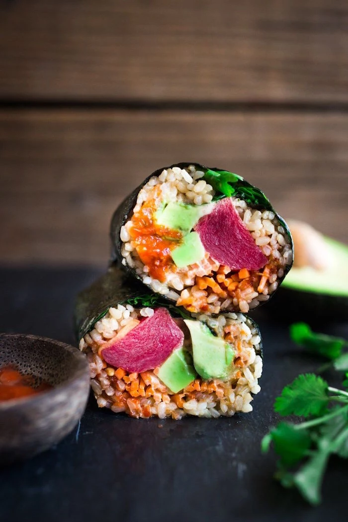 two sushi burritos with rice avocado parsley crab meat placed on black cutting board california roll recipe