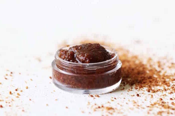 white background and surface small plastic container filled with diy lip scrub brown sugar around it