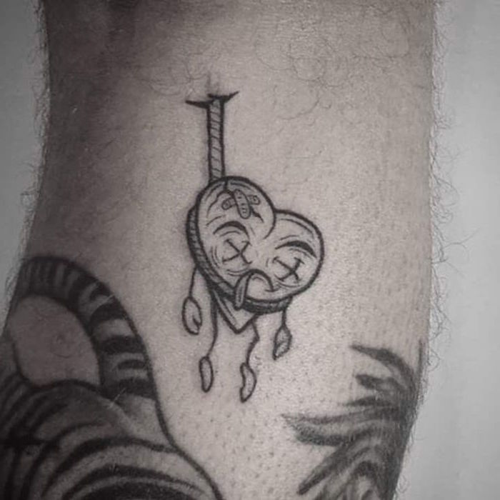 white background back of leg tattoo of dead broken heart heart finger tattoo hanging with rope with bandages