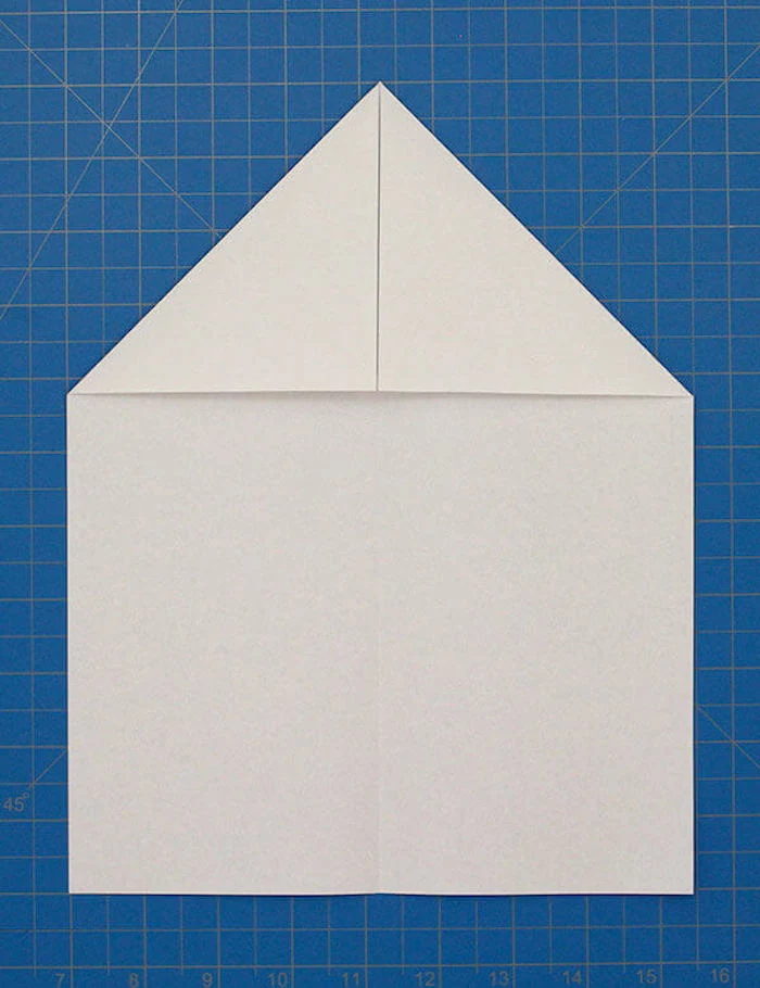 white piece of paper folded into a plane step by step paper airplane blue background diy tutorial