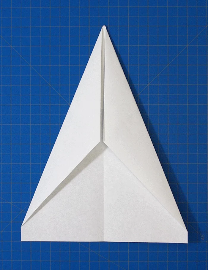 white piece of paper folded into a triangle on blue background step by step paper airplane