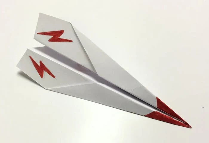 white piece of paper folded into plane simple paper airplane red flashes and red tip drawn on it placed on white background