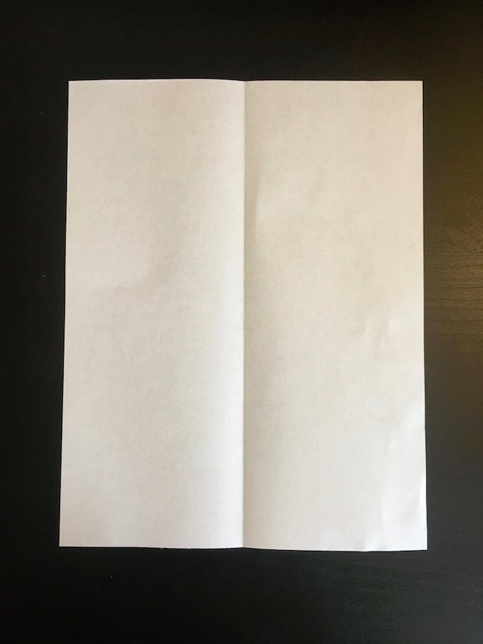 white piece of paper placed on black background folded in two and opened flat on the surface paper airplane folding