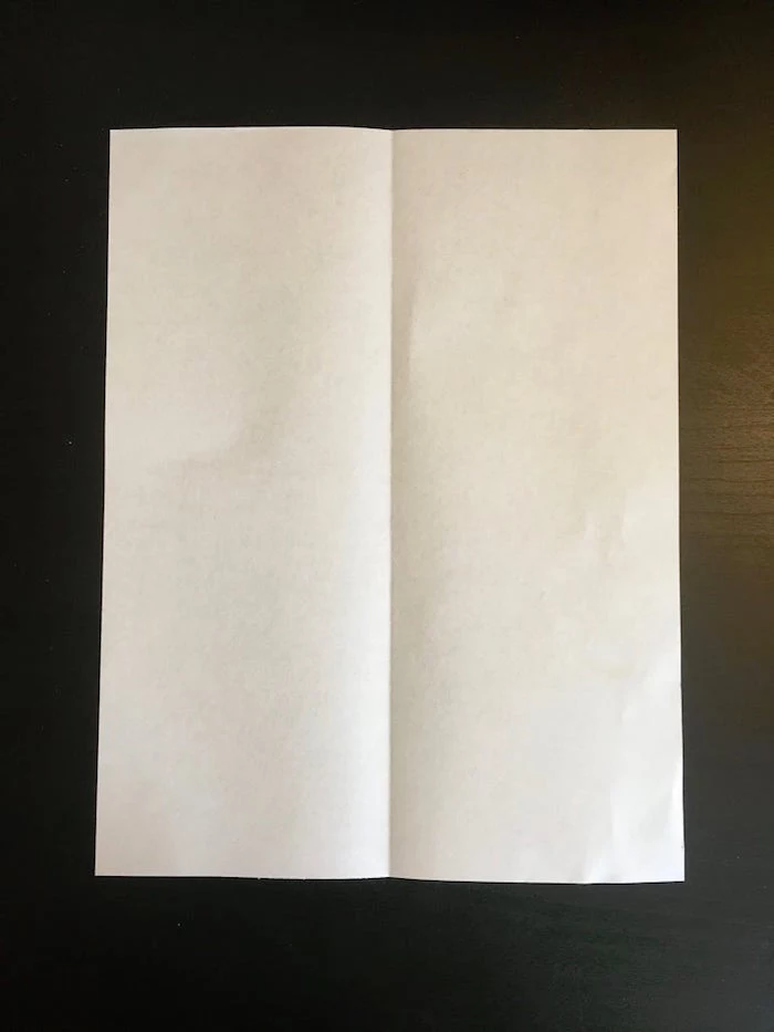 white piece of paper placed on black background folded in two and opened flat on the surface paper airplane folding