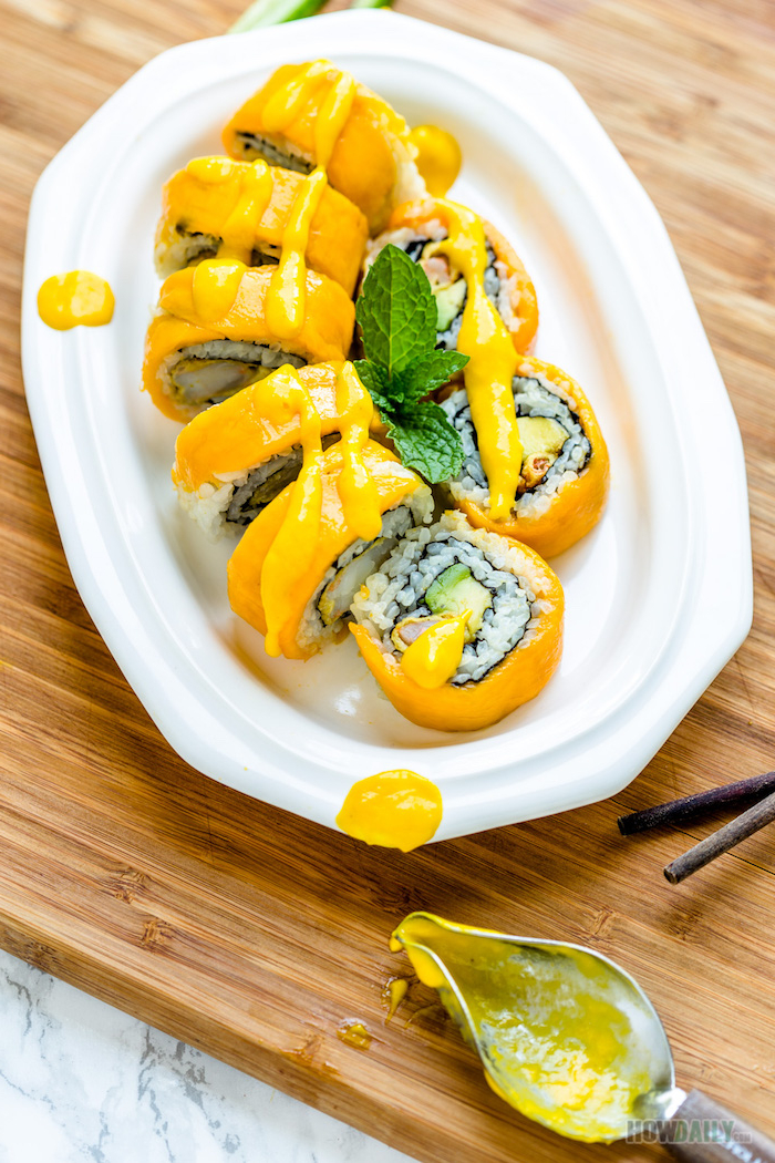 white plate with mango sushi in it with rice how to roll sushi decorated with mint leaves and drizzled with sauce