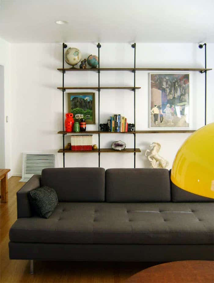 white walls with bookshelf made with industrial pipes mounted on it behind dark gray sofa