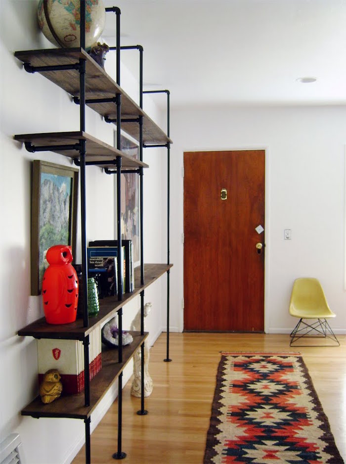 wooden door industrial pipes bookshelf mounted on white wall colorful rug on wooden floor