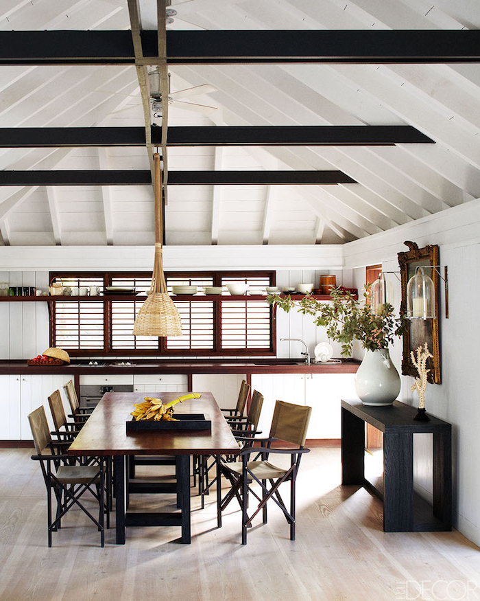 black exposed wood beams over long wooden dining table with black wooden chairs small beach house with cathedral ceiling