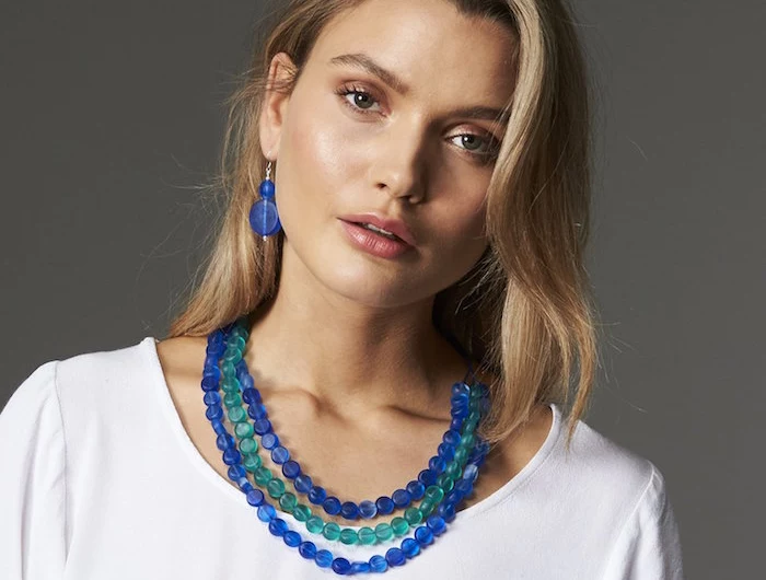blonde woman wearing resin earrings necklaces and rings in blue and turquoise wearing white blouse