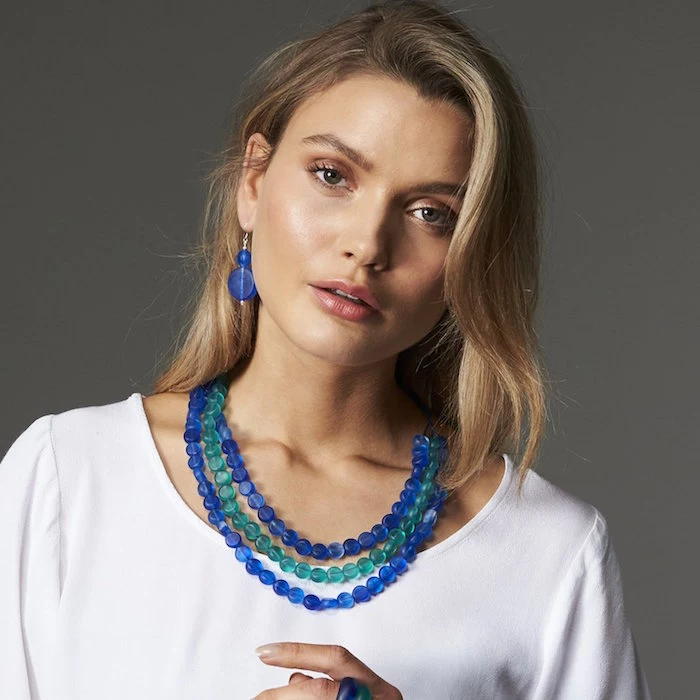 blonde woman wearing resin earrings necklaces and rings in blue and turquoise wearing white blouse
