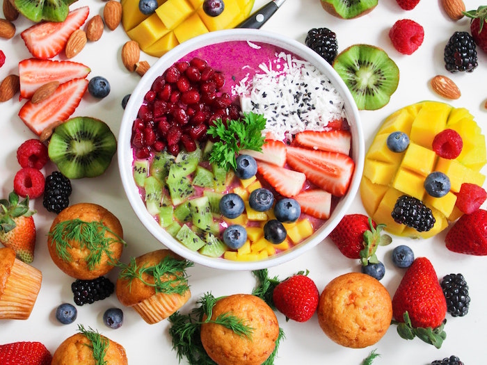 bowl full of fruits inflammatory foods smoothie bowl lots of fruits around it strawberry kiwi mango pomegranate seeds coconut blueberries