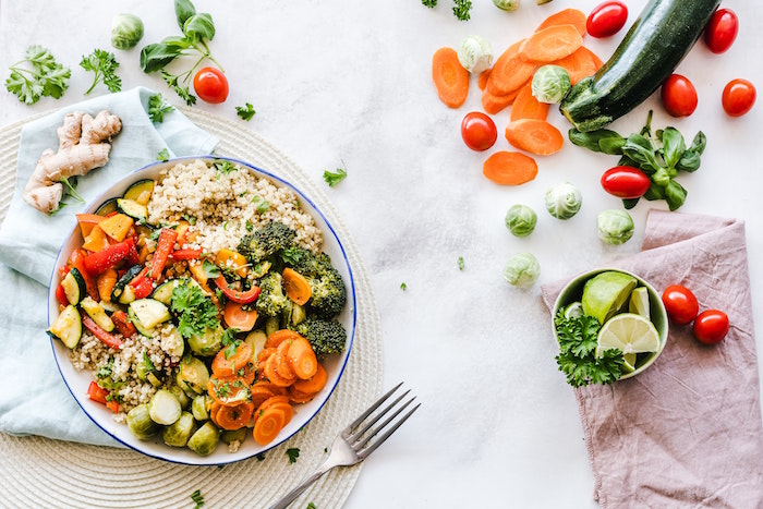 bowl full of quinoa carrots broccoli brussels sprouts peppers zucchini inflammatory foods lots of food scattered around it