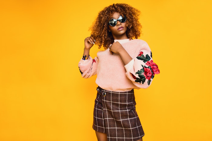 brown skirt and pink sweater worn by woman with brown curly hair keep your hair healthy yellow background