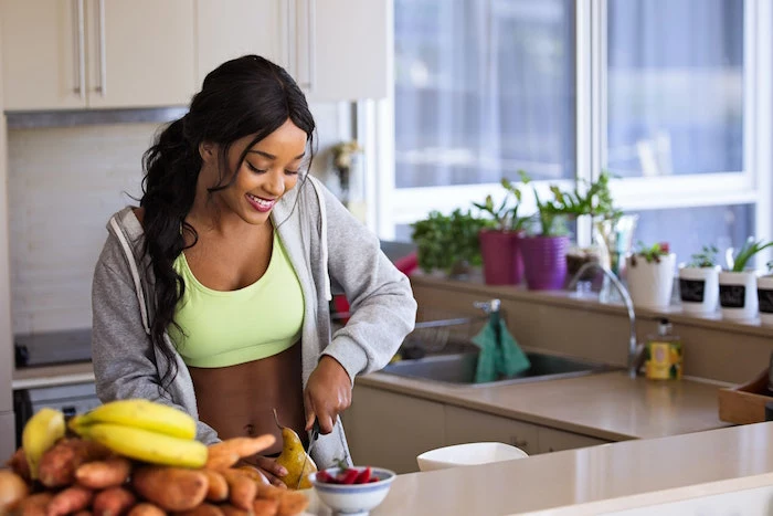 brunette woman wearing green sports bra gray hoodie standing next to kitchen counter cutting a pear inflammatory foods