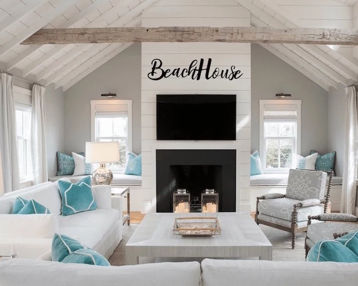cathedral ceiling with exposed wood beams coastal decor white sofas gray armchairs with blue throw pillows in front of fireplace
