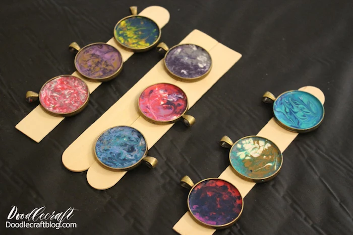 epoxy jewelry nine necklace pendants made with melted crayons in different colors and resin placed on wooden sticks