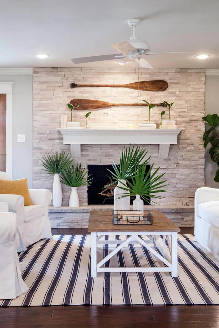fireplace decorated with stones two paddles on top coastal decor white armchairs and sofa in front of it with wooden coffee table
