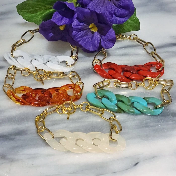 five golden chain bracelets with resin links in different colors resin jewelry red blue white orange resin placed on marble surface