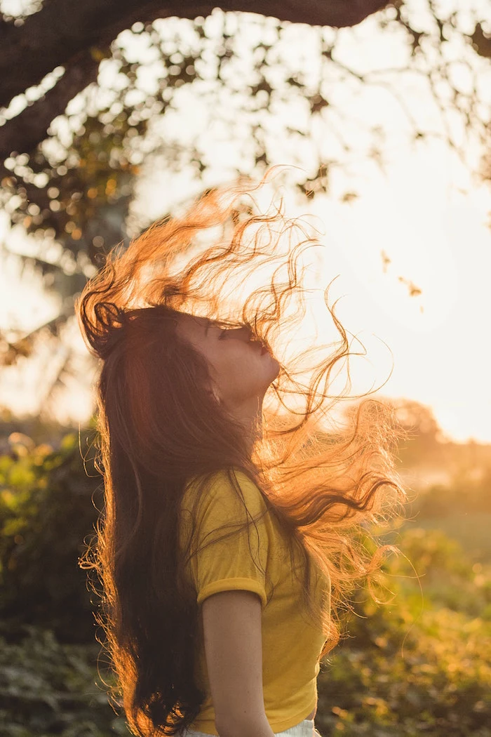girl with long brown wavy hair flipping it wearing yellow top standing in the sun keep your hair healthy