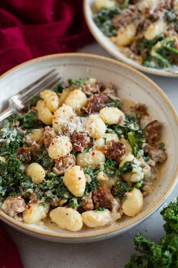 gnocchi with italian sausage and kale garnished with grated parmesan cheese easy gnocchi recipe in gray plate fork on the side