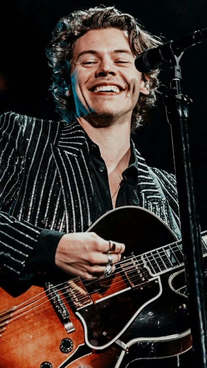 harry on stage smiling wearing black striped blazer harry styles aesthetic wallpaper playing the guitar