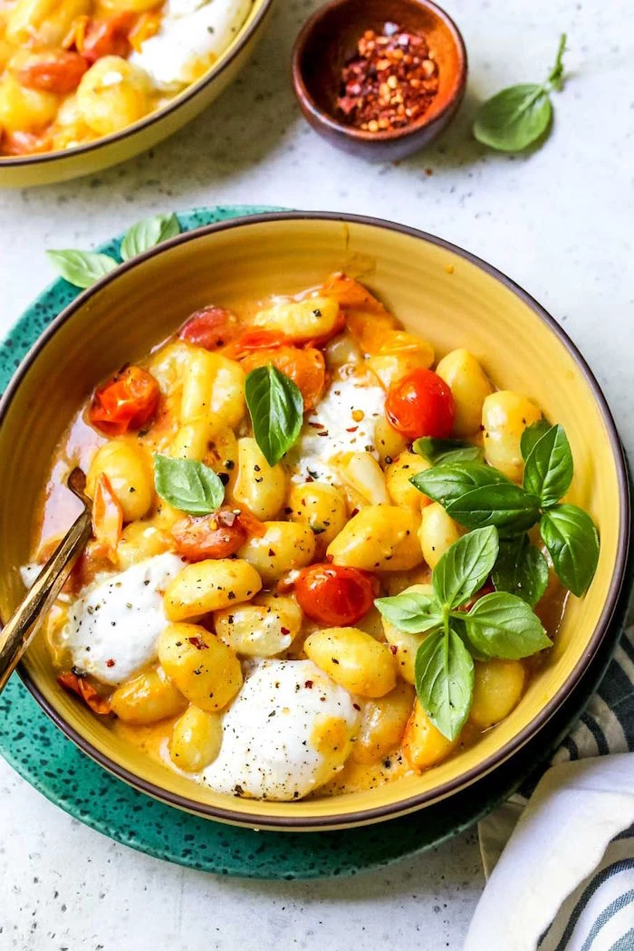 how to cook gnocchi yellow bowl full of gnocchi with cherry tomatoes burrata cheese garnished with fresh basil leaves