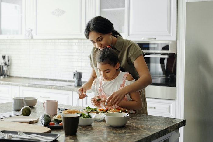 inflammatory foods mom and daughter standing next to kitchen island with granite countertop cutting up greens together