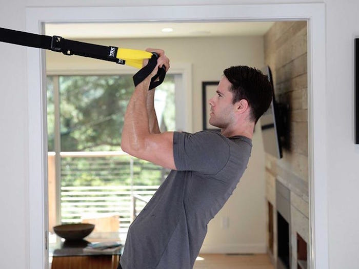 man wearing gray t shirt working out with elastics tied to the wall valentine's day gifts for men large tv screen in the background