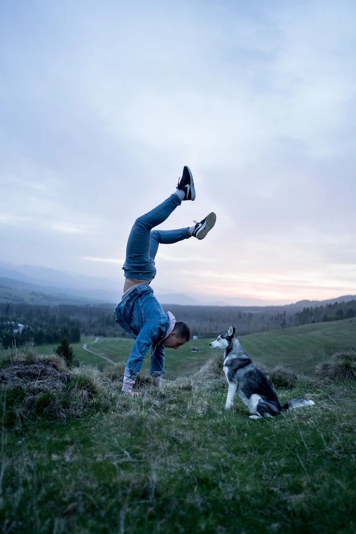 man wearing jeans pink hoodie denim jacket black sneakers doing a hand stand inflammatory foods black and white husky dog standing next to him