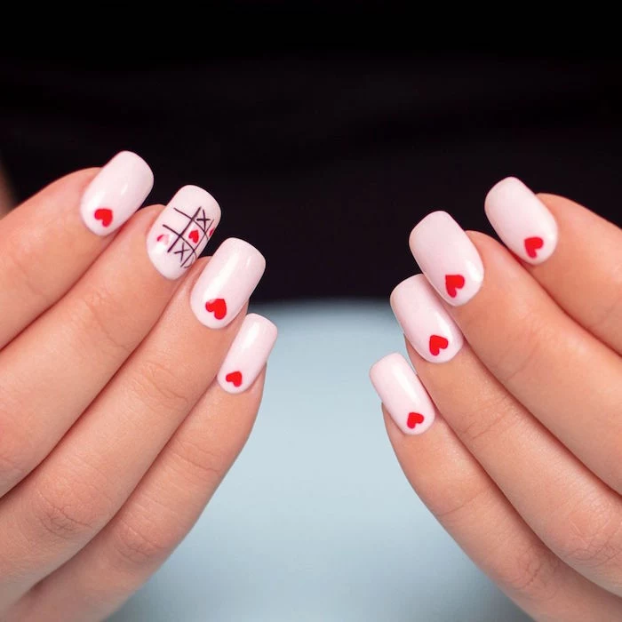 medium length squoval nails covered with white nail polish valentines day nails 2021 small red hearts on each nail tic tac toe decoration on middle finger