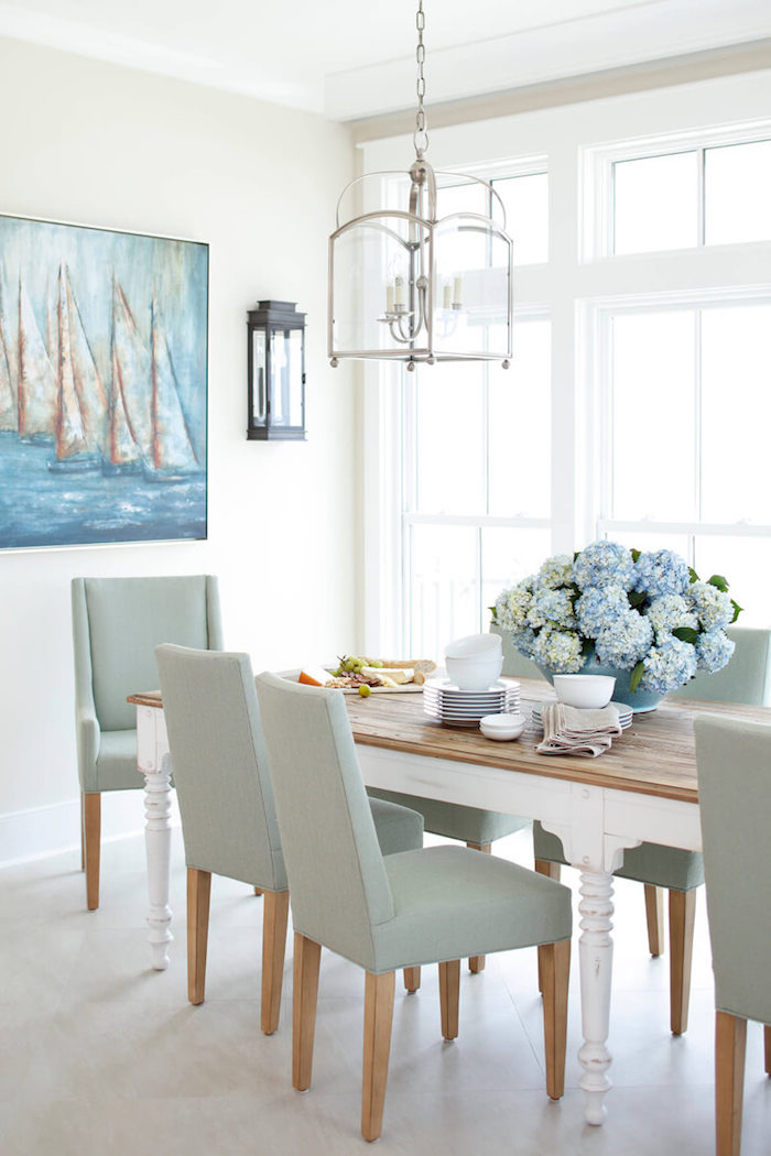 nautical decor gray chairs surrounding wooden dining table with large blue flower bouquet in the middle painting of boats in the sea on white wall