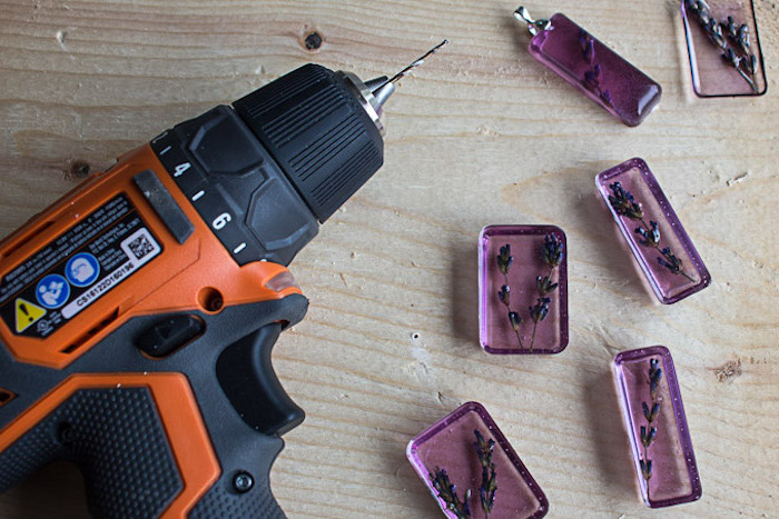 necklace pendants made with pink resin and dried lavender making resin jewelry placed on wooden surface next to drill