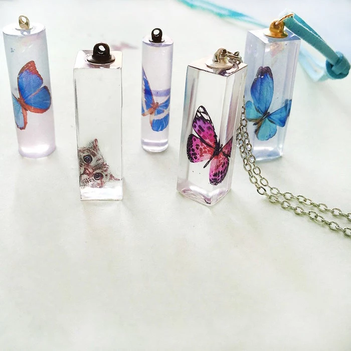 necklace pendants with paper butterflies and cat inside resin earrings in square and cilinder shapes placed on white surface