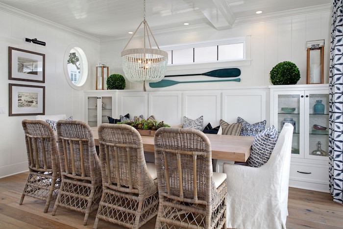 rattan chairs around wooden dining table next to bench with lots of throw pillows beach decor white walls two blue paddles hanging on the wall