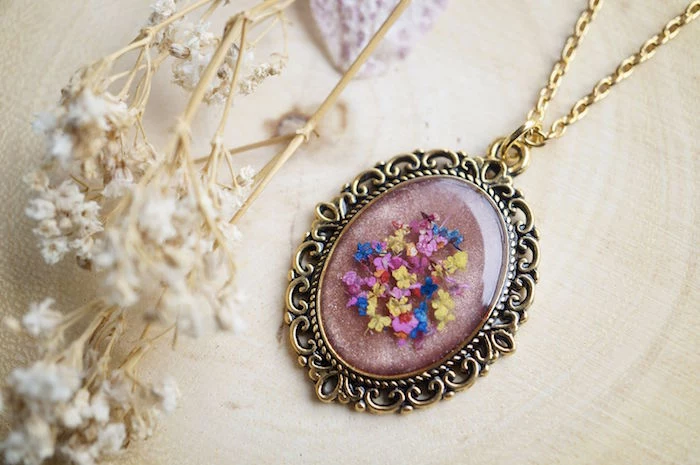 resin jewelry vintage necklace with dried flowers inside eliptical form gold necklace chain placed on white cloth next to dry flowers
