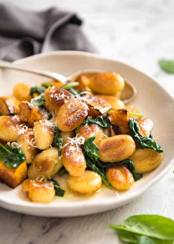 roasted pumpkin gnocchi with spinach garnished with grated parmesan cheese gnocchi recipe white plate on white wooden surface