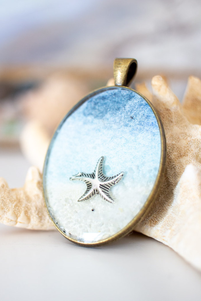 sea star placed inside bronze vintage necklace pendant with blue watercolor paper jewelry making for beginners