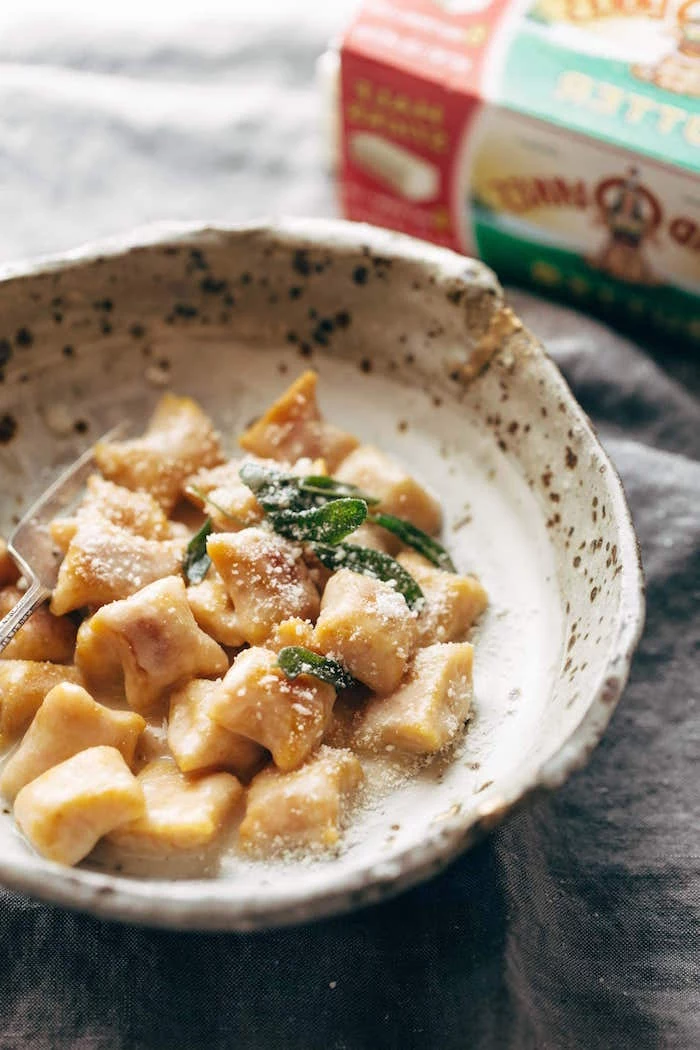small bowl filled with pumpkin gnocchi with cheesy sauce best gnocchi recipe garnished with fresh mint leaves grated parmesan cheese